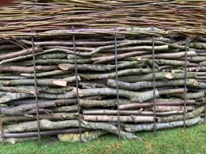 Cottage garden log stack 'dead hedge' with woven willow screen on top. 